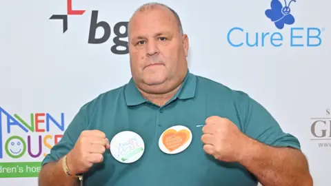 Getty Images A man wearing a teal shirt posts in from on a sponsor wall at a charity event