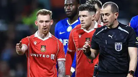 Lewis O'Brien of Wrexham speaks to Referee Peter Bankes as a VAR review takes place