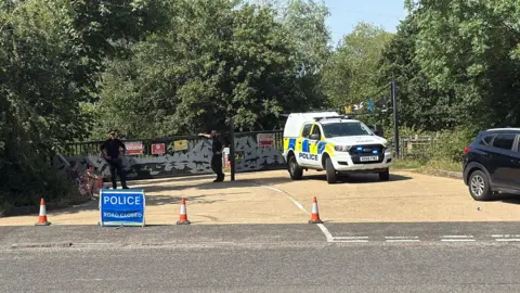 Police car and cones outside lake entrance.