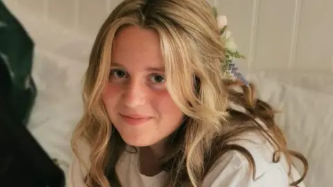 Chloe pictured wearing white t-shirt, and has a bow in her blonde hair. She is smiling at the camera