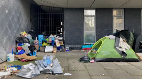 A green domed tent next to piles of rubbish outside a metal gated alleyway 