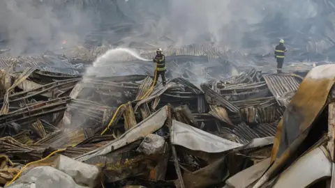 EPA/Shutterstock Rescuers work at the site of a Russian missile strike on a goods storage in Kyiv. A large stream of water can be seen coming from a hose one of the individuals is holding.