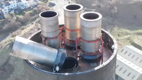 Drone shot of the top of the stack of Peel Power Station. It shows four flue caps with one leaning against the rim of the top secured with ropes.