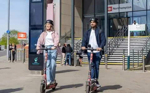 West Northamptonshire Council A man and a woman on e-scooters outside Northampton railway station