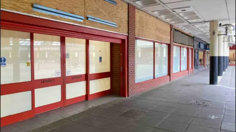 A red shopfront with obscured windows and doors with a white covering on the inside, and its shop sign removed