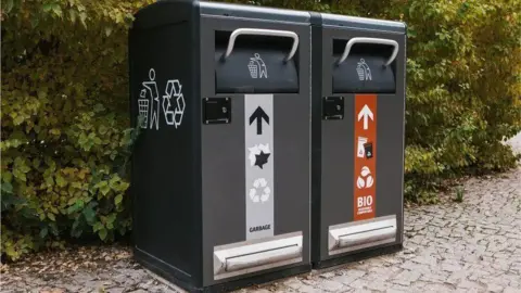 Two black solar powered bins - one has a red stripe on for recycling and one has a grey stripe on general rubbish.