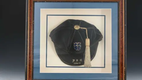 Kinghams Auctioneers A blue velvet cap with a pale tassel, framed in a wooden picture frame.