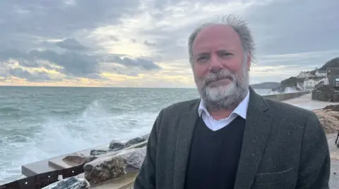 Julian Brazil stood to the right of a damaged sea wall in Torcross.