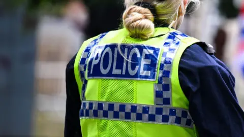 The back of a female police officer's fluorescent jacket 