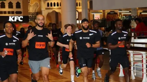 Hermen Dange People in black t-shirts run through a shopping centre. 