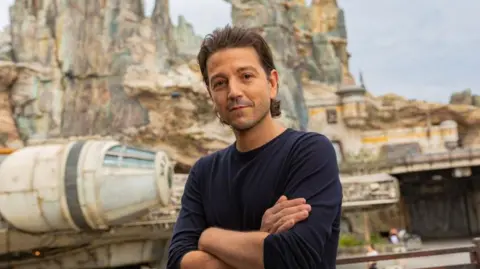 Getty Images Diego Luna standing with his arms crossed in front of a space ship on set