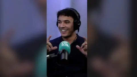 Freddie Fraser smiling in front of a green mic, wearing headphones.