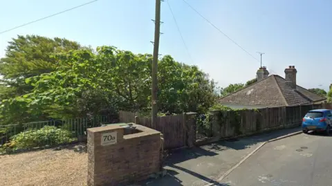 google maps The house as viewed from the road. Its roof is visible over the fence, but the rest is further down the cliff out of sight.