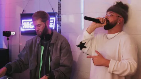 Firmative Media MC Window Kid and DJ and producer Nathan Dawe behind the counter of a chip shop