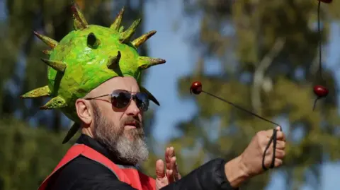 Reuters A man with a greying heard wearing sunglasses and a hat shaped like a green conker shell