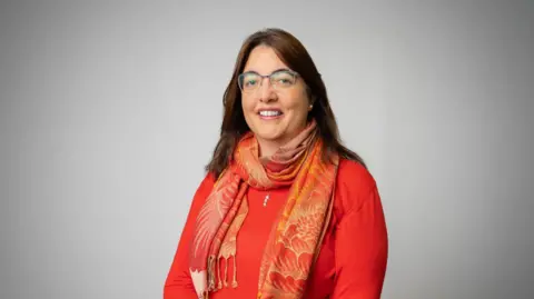 Government of Jersey Woman in glasses in orange scarf and orange top looks into the camera