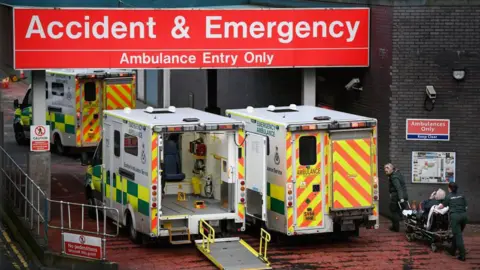 Getty Images Three ambulances queued up outside the accident and emergency entrance at the Glasgow Royal Infirmary. Two paramedics can be seen dragging a man on a stretcher into the hospital. 