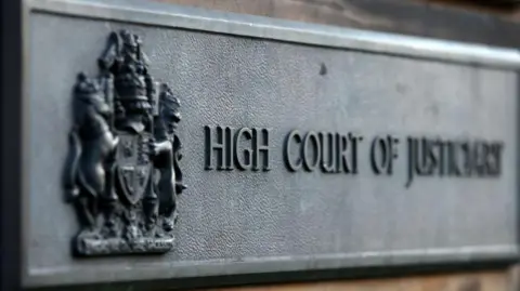 A grey 'HIGH COURT OF JUSTICIARY' sign at the High Court in Edinburgh.
