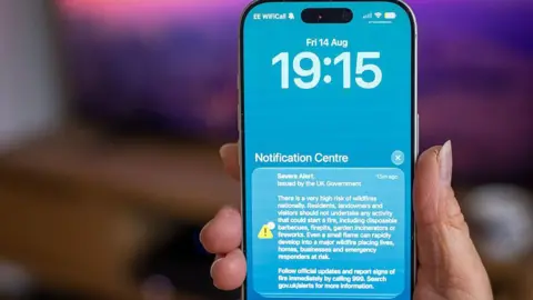 A picture of a phone with blue background carrying the UK government Severe Alert warning of the risk of wildfires.