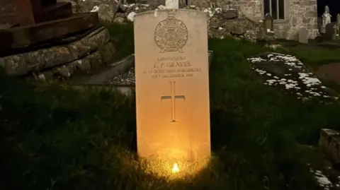 War grave lit up, behind it is a church