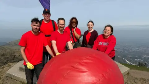 The BBC Hereford & Worcester team stood on the Worcestershire Beacon around the giant red nose. The six members of the team are wearing red clothing.