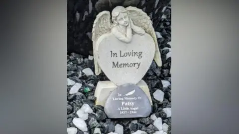Annie Kalotschke A stature with an angel praying above a heart with a stone with the words Patsy. A little angel