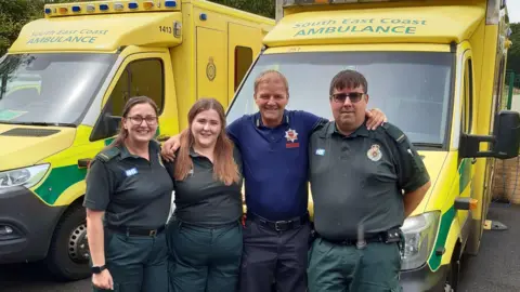 Secamb Scott Saunders stands in front of an ambulance with three paramedics