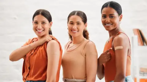 Three women with plasters on their left arms.