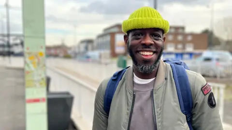 Raph Adams stands in the street, smiling.