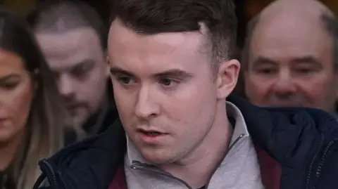 PA Media Ryan Casey. He has short dark hair, wearing a navy coat and grey half zip.