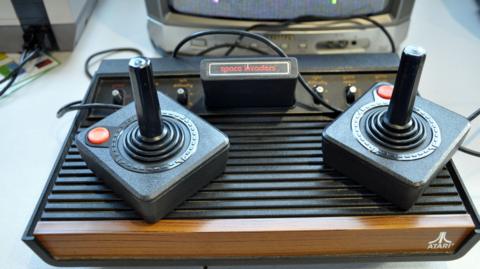 An Atari games console, with two joysticks, a Space Invaders cartridge and a fake wood veneer.