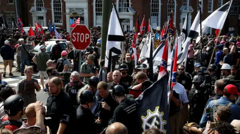 Reuters Penganut supremasi kulit putih, mengenakan pakaian hitam, seragam dan helm Nazi, berunjuk rasa di Charlottesville, Virginia pada tahun 2017, sambil membawa bendera Konfederasi dan bendera hitam putih