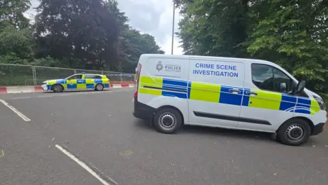 A police car and a crime scene investigation van are parked on a road.