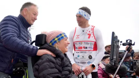 PA Media Sinfield speaks to a man who assisted a woman in a wheelchair with MND during a running event