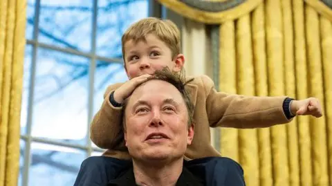 Getty Images Elon Musk's son, X, sits on his shoulders in the Oval Office