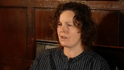 Professor Wells sat inside a pub speaking to a reporter, who is not pictured. She has curly brown hair and is wearing a striped shirt.