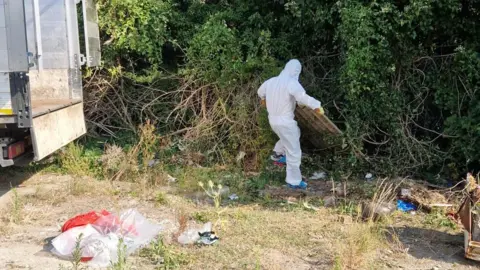 Helen John A waste removal worker in protective clothing clears vegetation and debris during the fly-tip clean-up.