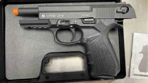 National Crime Agency A close-up of a black handgun with an orange tip in a black box. 