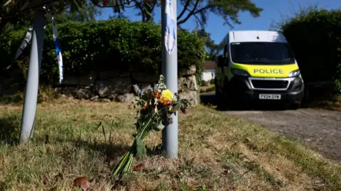 Flowers and a police vehicle outside the home of 78-year-old former government minister Ann Widdecombe after she was found dead, in Haytor, Britain, July 11, 2026. 