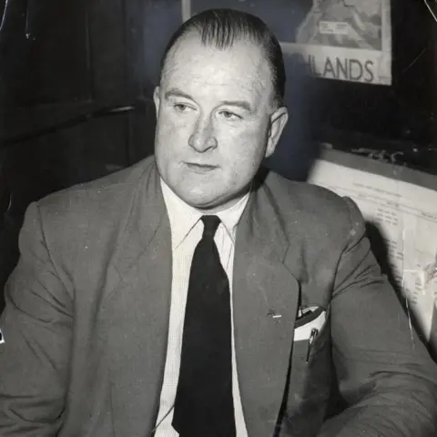 Getty Images William Watt is a balding man in a grey suit with white shirt and dark tie. He is sitting, looking off-camera.