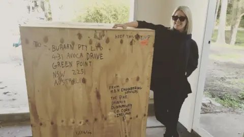 Cherie Reid Karina Reid standing next to the crate the bell was transported in. She is leaning against the crate and smiling.