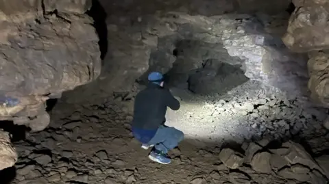 Bloxham Underground Tunnel Society A man kneeling down, shining a light further down the tunnel.