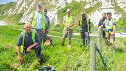 Seven men all in hi-vis jackets stand in front of the White Cliffs of Dover