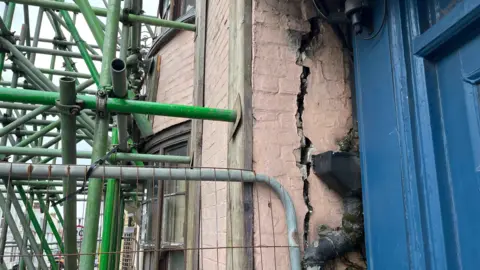 George Carden/BBC A crack about 3 foot long and a couple inches wide on the front façade of the building. Scaffolding can also be seen propping up the building.