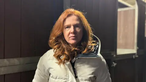 A woman with red hair looking at the camera, she is wearing a white coat