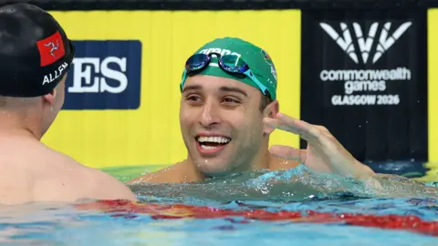 Getty Images Chad le Clos smiles in a swimming pool. He is wearing goggles and a green swimming cap.