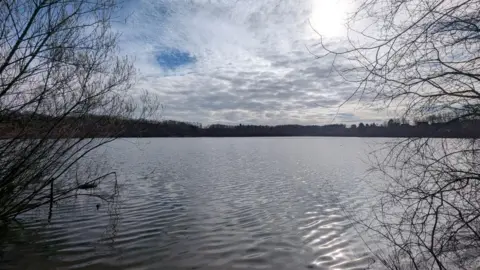 LDRS A large mere in the middle of a country park. Trees can be seen surrounding the shoreline.