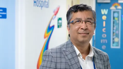 University Hospitals of Leicester NHS Trust Nitan is stood in the ward. He is wearing glasses and a jacket. 