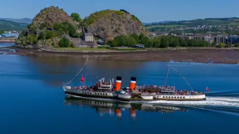 PA Media On a cloudless day, The Waverley is shown sailing along the River Cylde past Dumbarton Rock. The water is totally calm.