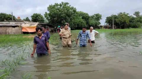 Gujarat Information/X Rescue officials help evacuate people in Surajgarh village of Nalsarovar area as flood waters rise above the knee